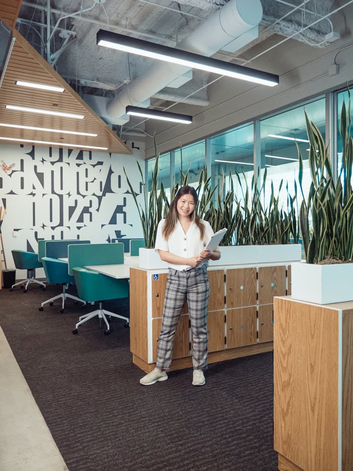 Asian woman standing in a stylish office with modern decor holding documents.